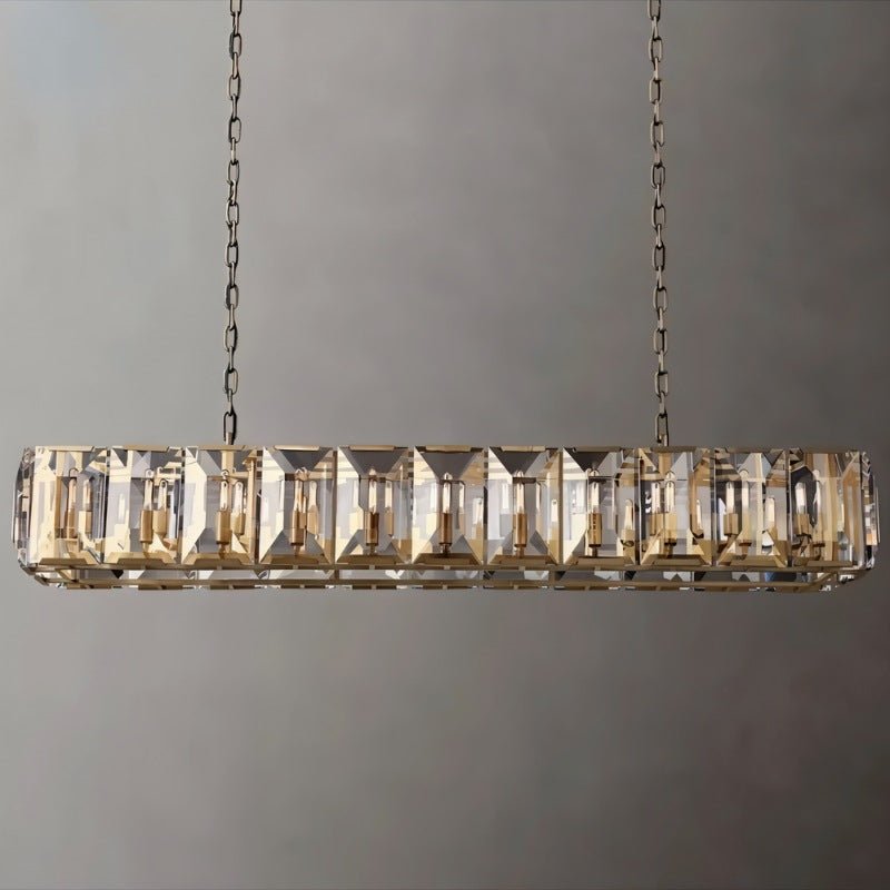 Linear chandelier with brass finish and stacked crystal prisms, suspended by chains against a neutral gray wall.