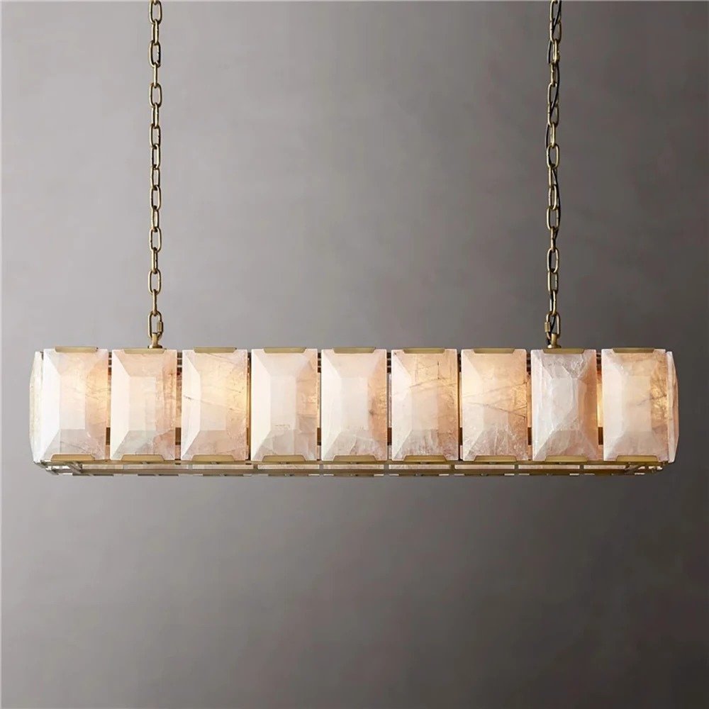 Linear chandelier with brass finish and stacked alabaster stone panels suspended by chains against a gray wall.