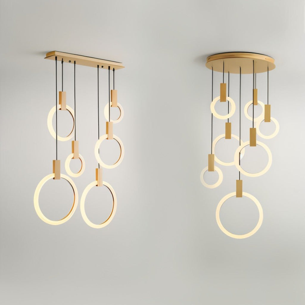 Modern pendant chandelier with warm brass finish and illuminated ring-shaped LED lights suspended from wooden dowels against white background.